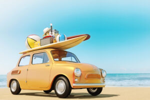 Small retro car with baggage, luggage and beach equipment on the roof, fully packed, ready for summer vacation, concept of a road trip with family and friends, dream destination, very vivid colors with dominant blue sky and ocean and bright orange car.